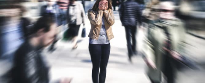 Woman clutching her face and suffering from a panic attack in a busy public square