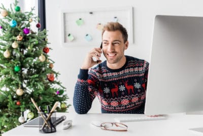 Smiling businessman in christmas sweater talking on the phone with a christmas tree in the background